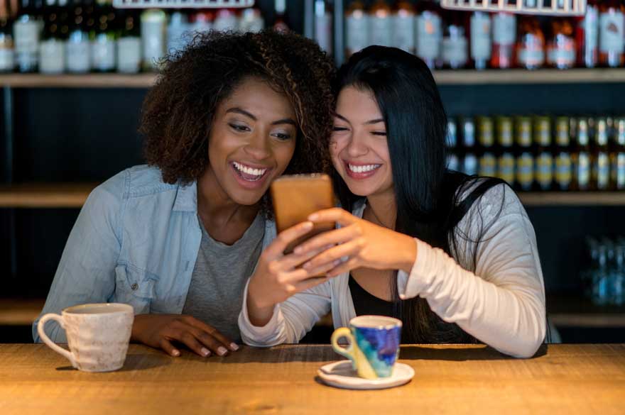 two women looking at mobile phone over coffee