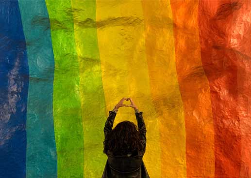Girl making a heart hand gesture under a rainbow flag
