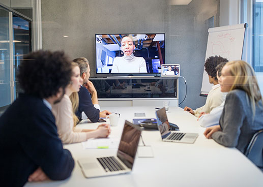 People around a conference table interacting with team members onscreen