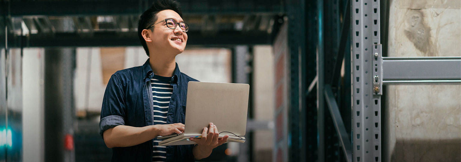 Man in warehouse holding laptop smiling