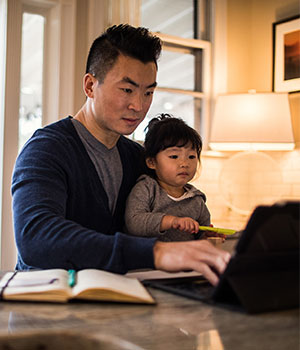 man sitting at home with small child on lap working at laptop