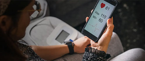 Young woman measures blood pressure sitting on sofa at home with smartphone connected to device