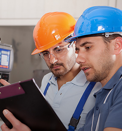 two manufacturing workers in helmet and looking at their notes