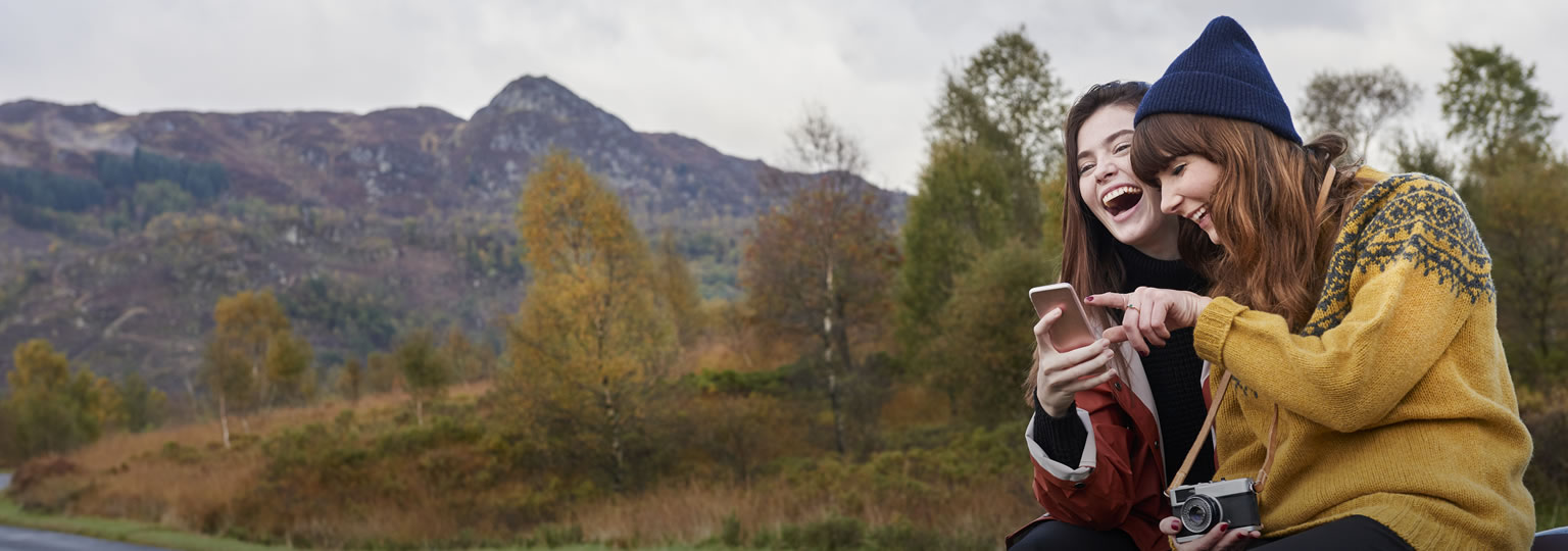 two women in the mountains laughing with a smartphone