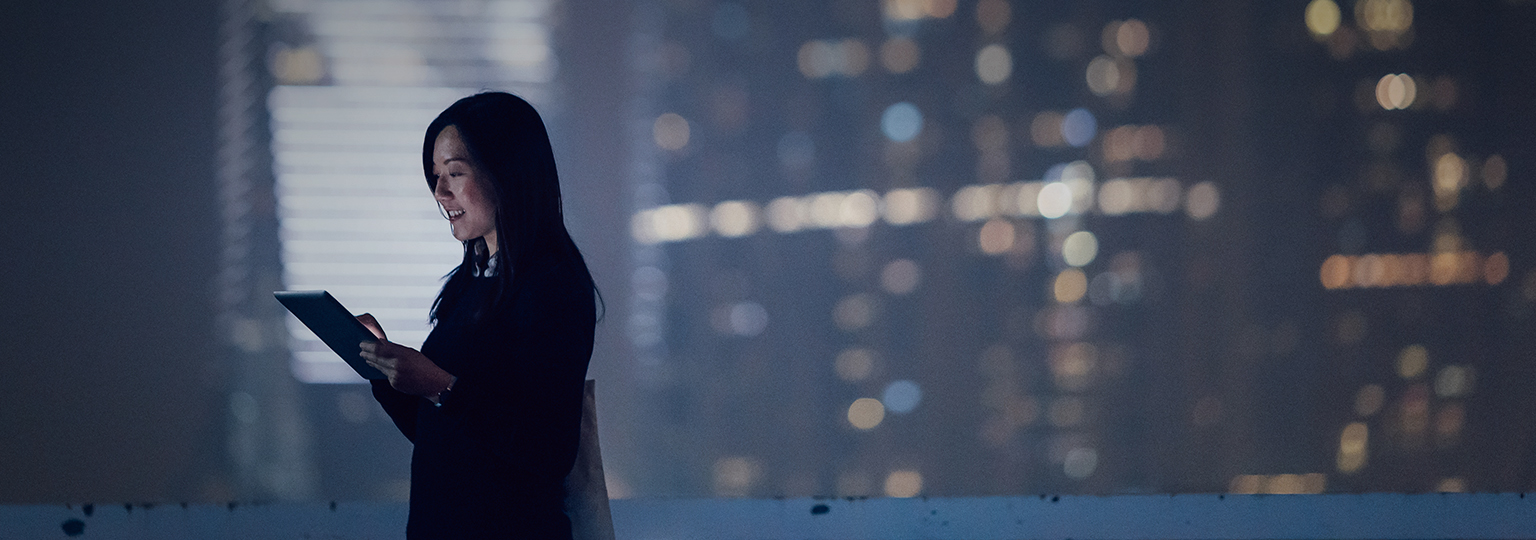 woman working on tablet with city light behind her