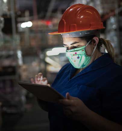 woman wearing hard hat and mask working on tablet