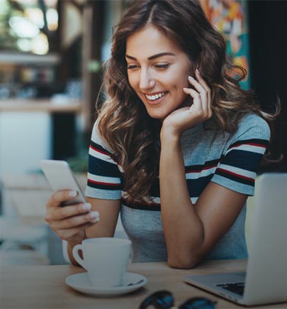 lady smiling and looking at her mobile while having coffee